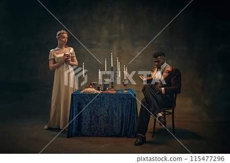Woman in satin dress holds wine glass, standing beside candlelit table, while man in vintage attire reading book against retro tapestry background Woman in satin dress holds wine glass, standing beside candlelit table, while man in vintage attire reading book against retro tapestry background 115477296