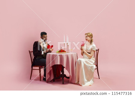 Historical scene with couple in Renaissance attire, enjoying moment of flirt, sharing hearts that signify love against pink studio background 115477316