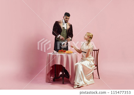 Portrait of handsome man and elegant woman in image of Viscount and Viscountess dining together, drinking tea against pink studio background 115477353