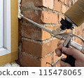 Window installation. The process of insulating windows with construction foam. A builder's hand seals the cracks between the building and the window frame. Construction and insulation of the building. 115478065