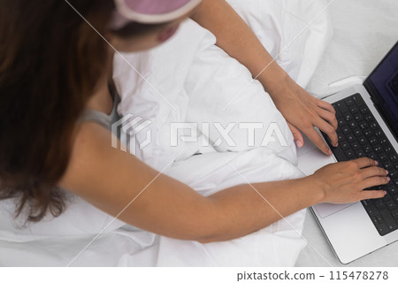 Close-up: Female hands actively engaging in online social networking from home, working and connecting through a laptop in bed.  115478278