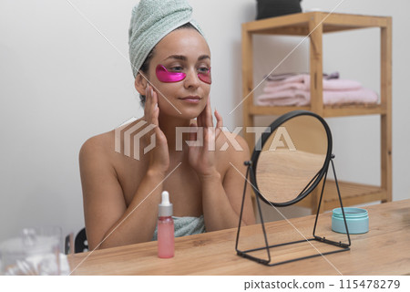 A woman, absorbed in her reflection, amplifies her skincare with professional cosmetics, placing pink under-eye patches for a rejuvenating experience A woman, absorbed in her reflection, amplifies her skincare with professional cosmetics, placing pink under-eye patches for a rejuvenating experience 115478279