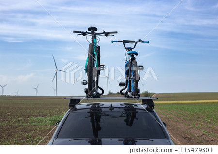A car is transporting bicycles on the roof with two bicycles fastened. Behind there are windmills A car is transporting bicycles on the roof with two bicycles fastened. Behind there are windmills 115479301