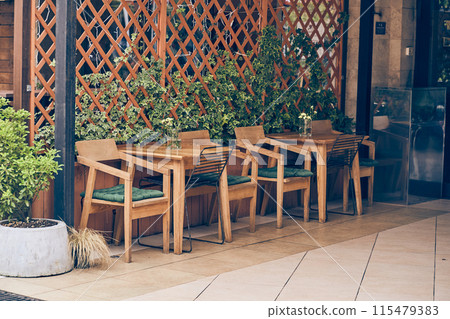 An empty cafe terrace with a wooden table and chair. A cozy street with flowers and a table, facade decor with space to copy. High quality photo An empty cafe terrace with a wooden table and chair. A cozy street with flowers and a table, facade decor with space to copy. High quality photo 115479383