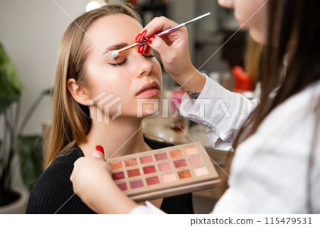 Skilled woman softly blends outer edges of eyeshadow. Professional artist ensures look uniquely suited to lady client personal style 115479531