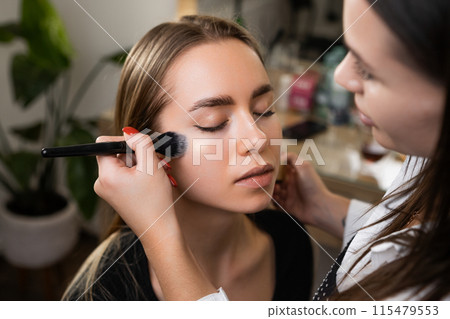 Makeup artist lightly applies highlighter with special brush on client face.  115479553