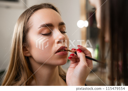 Woman blends lipstick with previously applied lip pencil. Lip brush technique results in polished and sophisticated lip look on client face Woman blends lipstick with previously applied lip pencil. Lip brush technique results in polished and sophisticated lip look on client face 115479554
