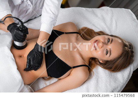 Employing an ultrasound device, the cosmetologist administers a lifting procedure on the womans belly 115479568