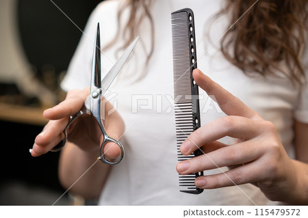 Female hairdresser holding scissors and comb in her hands.  115479572