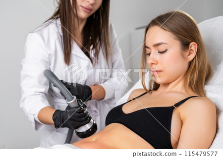 Lady adjusts hair during vacuum cavitation procedure. Client happy to notice improvements in skin texture and elasticity in treated belly area 115479577
