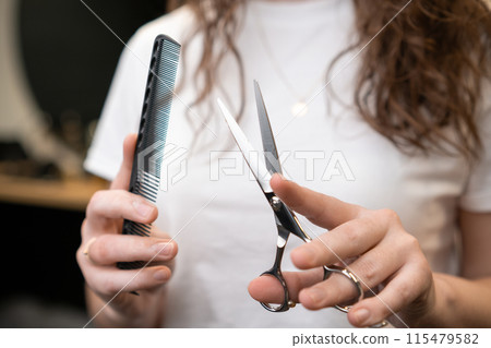 Hairdresser holding a comb and scissors in her hands standing in the salon. Hairdresser holding a comb and scissors in her hands standing in the salon. 115479582