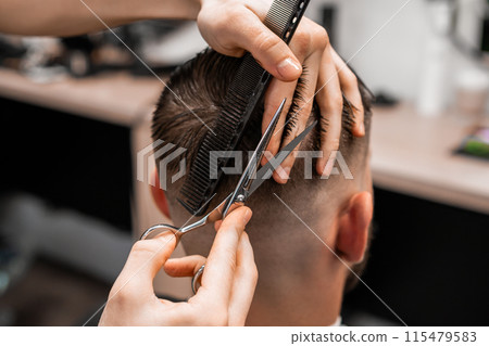 Barber uses scissors and a comb to cut the hair on the back of a man's head in a barbershop. Barber uses scissors and a comb to cut the hair on the back of a man's head in a barbershop. 115479583
