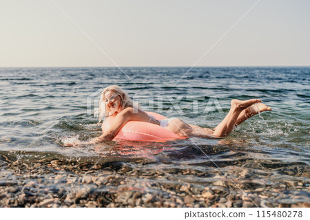 A woman is in the ocean, holding a pink inflatable tube A woman is in the ocean, holding a pink inflatable tube 115480278
