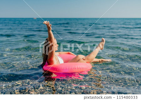 A woman is floating on a pink inflatable raft in the ocean 115480333