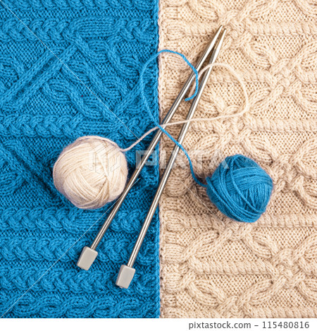 Two balls of thread and knitting needles on turquoise and beige knitted fabric. Concept of spending time at home and knitting warm clothes for winter and autumn. Heart made of threads Two balls of thread and knitting needles on turquoise and beige knitted fabric. Concept of spending time at home and knitting warm clothes for winter and autumn. Heart made of threads 115480816