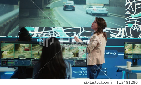Manager supervising diverse employees operators in delivery call center office, people using global positioning system to guide shipment cars on city routes via satellite navigation map. Camera A. 115481286