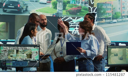 Diverse employees group discussing ways to speed up order delivery, looking for routes to avoid traffic on satellite navigation. Agency operators use CCTV footage in monitoring room. Camera A. 115481287