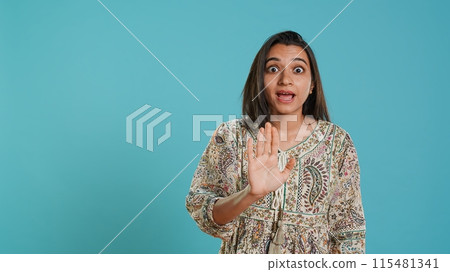 Stern indian woman doing stop hand gesture sign, complaining. Authoritative person doing firm halt sign gesturing, wishing to end concept, isolated over studio background, camera A 115481341