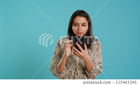 Woman scrolling on smartphone screen, doing online shopping, amazed by beautiful clothes. Portrait of relaxed person browsing internet websites, exclaiming in astonishment, studio background, camera A Woman scrolling on smartphone screen, doing online shopping, amazed by beautiful clothes. Portrait of relaxed person browsing internet websites, exclaiming in astonishment, studio background, camera A 115481345