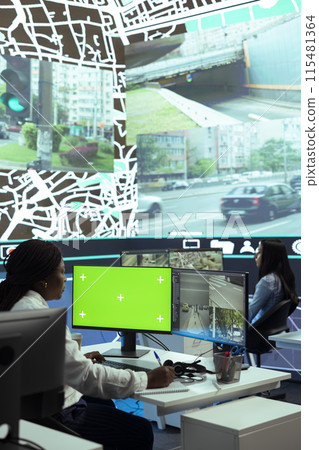 African american woman operator monitoring couriers in traffic via CCTV footage, using an isolated screen in control center. Dispatch employee uses gps coordinates to track cars. African american woman operator monitoring couriers in traffic via CCTV footage, using an isolated screen in control center. Dispatch employee uses gps coordinates to track cars. 115481364