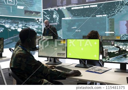 Army personnel monitors isolated green screen and surveillance footage, gathering important battlefield information. Trooper examines CCTV reconnaissance imagery to support soldiers. 115481375