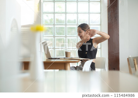 A woman is sitting at a table with a laptop and a cup of coffee. She is smiling and she is enjoying her time. The scene suggests a relaxed and comfortable atmosphere A woman is sitting at a table with a laptop and a cup of coffee. She is smiling and she is enjoying her time. The scene suggests a relaxed and comfortable atmosphere 115484986