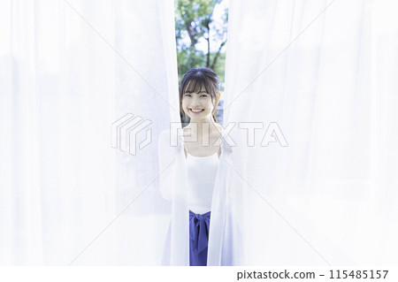 一個年輕女子從窗簾中探出頭來 115485157