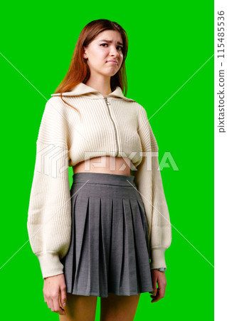 Displeased Young Woman Standing Against a Green Background Wearing a Crop Top and Skirt 115485536