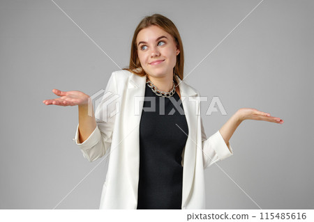 Young Woman Expressing Confusion With Hands Raised Against a Grey Background Young Woman Expressing Confusion With Hands Raised Against a Grey Background 115485616