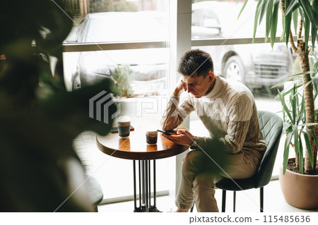 Young Man Engrossed in Smartphone at a Modern Cafe During Daytime 115485636