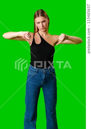 Young Woman Expressing Disapproval With a Thumbs Down Gesture Against a Green Background 115485637