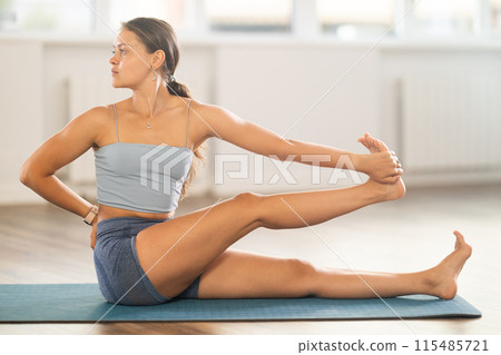 Sportive girl practicing seated hand to toe pose of yoga in light room 115485721