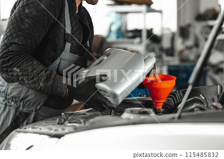 Close up of car service worker pouring new oil into car engine Close up of car service worker pouring new oil into car engine 115485832
