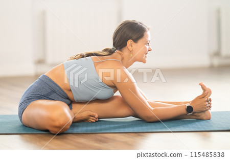 Positive young woman doing stretching asana Janu Sirsasana Positive young woman doing stretching asana Janu Sirsasana 115485838
