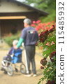 An elderly man in a wheelchair walking in a flower-filled park with a caregiver assisting him 115485932
