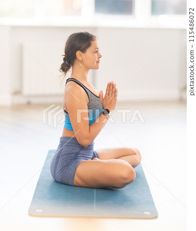 Sportive girl practicing lotus pose of yoga in light room 115486072