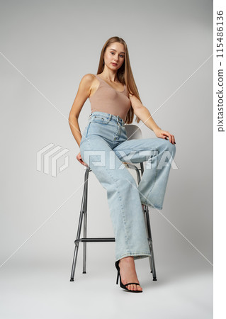 Young Woman Sitting on Stool in High Rise Jeans on gray background 115486136