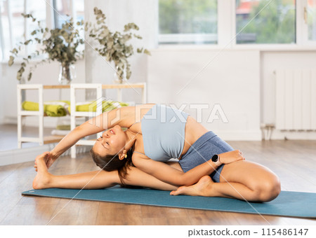 Young slim woman doing stretching in Parivrtta Janu Sirsasana asana 115486147