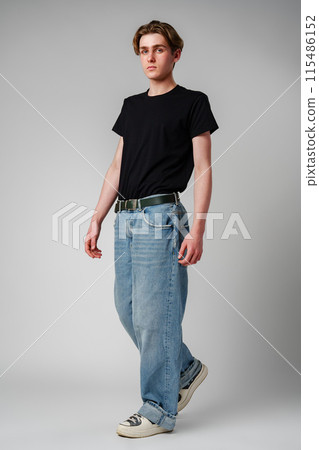 Casual Young Man Standing in Studio With Neutral Background Wearing Jeans and Black T-Shirt Casual Young Man Standing in Studio With Neutral Background Wearing Jeans and Black T-Shirt 115486152