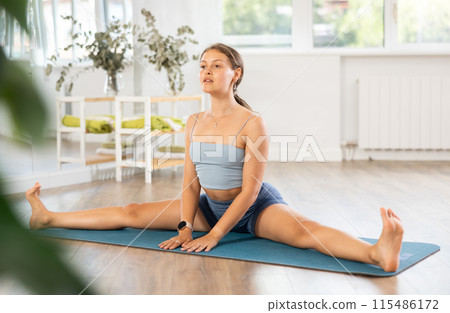 Young fit woman performing Upavistha Konasana on yoga mat 115486172