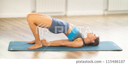 Sportive girl practicing bridge pose of yoga in light room 115486187