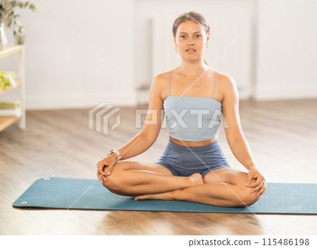 Sportive girl practicing lotus pose of yoga in light room 115486198
