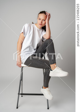 Curly girl model posing on a chair against gray background 115486203