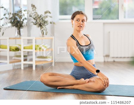 Young woman practicing parivritta sukhasana yoga pose 115486207