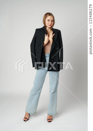 Young Woman Wearing Black Jacket and Jeans posing on gray background studio shot . Young Woman Wearing Black Jacket and Jeans posing on gray background studio shot . 115486279