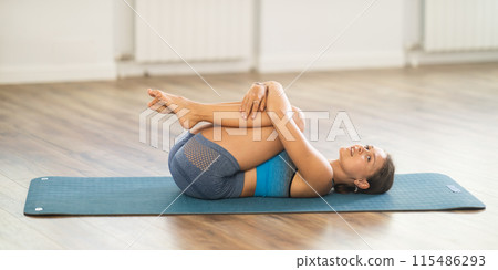 Pawanmuktasana yoga pose performed by slender girl in gym 115486293