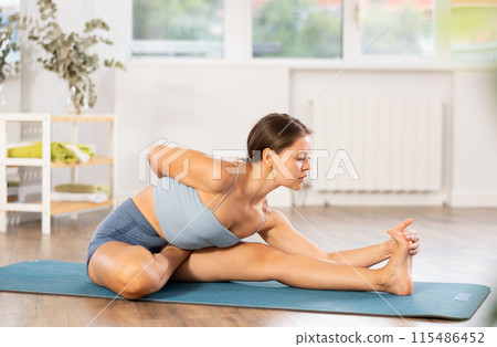 Positive young woman doing stretching asana Janu Sirsasana Positive young woman doing stretching asana Janu Sirsasana 115486452