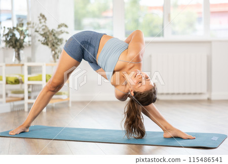 Young woman performing Bound Triangle yoga Pose in bright room 115486541