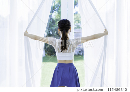 Rear view of a young woman opening lace curtains 115486840