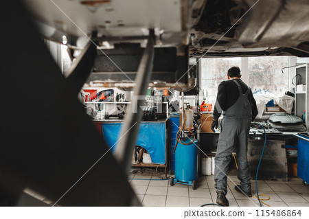 Workman mechanic working under car in auto repair shop Workman mechanic working under car in auto repair shop 115486864